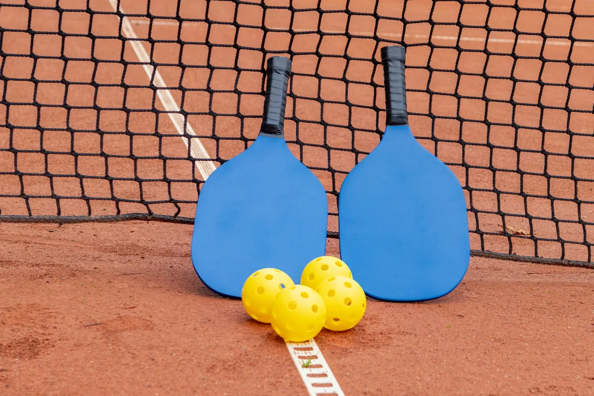 Raquettes de pickleball et balles perforées posées au sol devant un filet