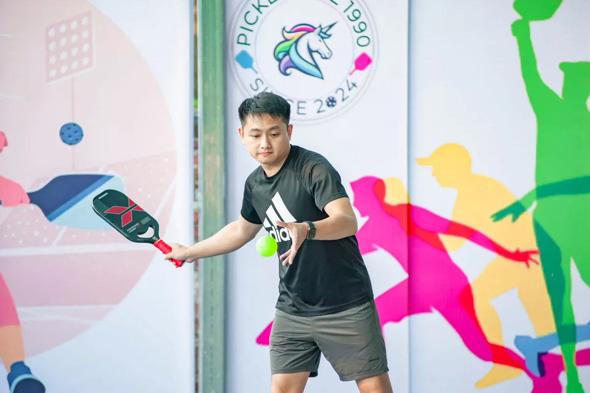 Joueur de pickleball en plein échange, raquette pleine et balle perforée, sur un court intérieur