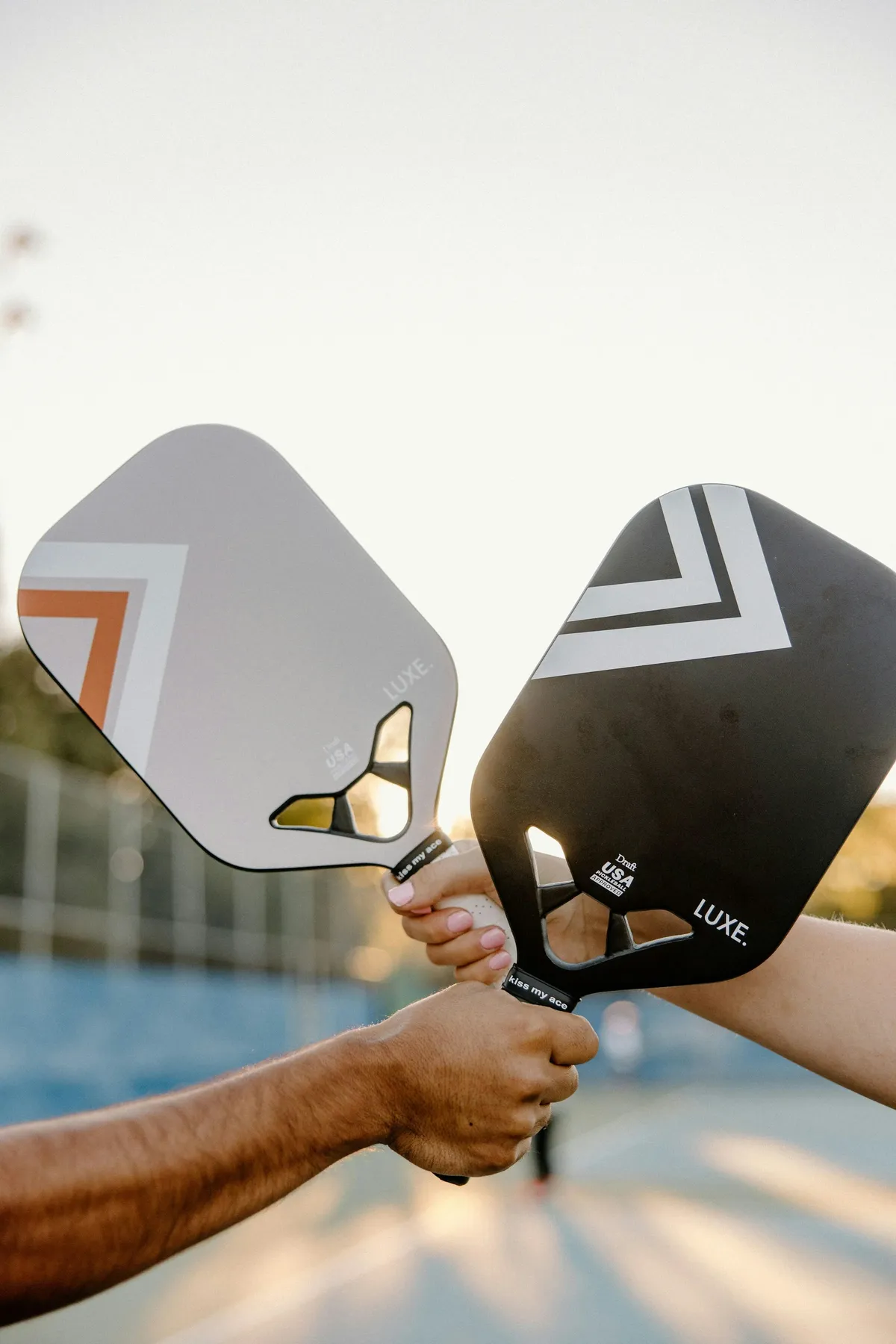 Deux joueurs de pickleball font se toucher leurs raquettes sur un court extérieur