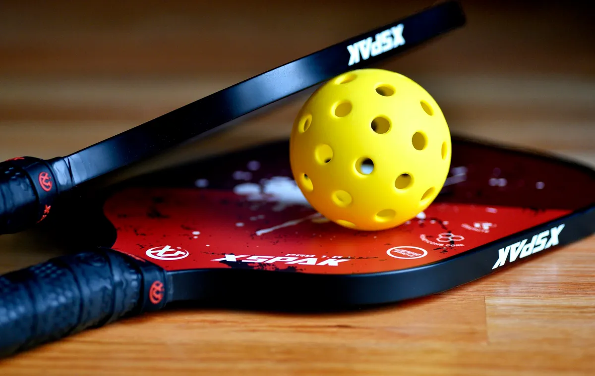 Gros plan sur une balle de pickleball perforée posée sur une raquette pleine